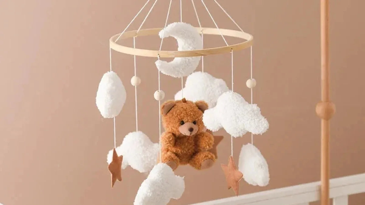 Mobile ours et nuages en bouclette suspendu à un anneau en bambou, le bras en bois du support à droite, au-dessus de la barre d'un lit blanc