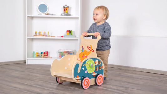 Enfant debout qui pousse un chariot de marche en bois en forme d'éléphant, les deux mains sur la poignée, dans une chambre claire