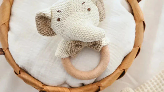 Hochet crochet en coton à tête d'éléphant sur un anneau en bois, posé sur un linge blanc dans un panier en osier