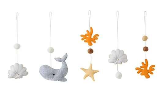 Cinq jouets en feutrine gris, blanc et orange, une baleine, une étoile, des coraux et des coquillages, chacun sur un cordon blanc