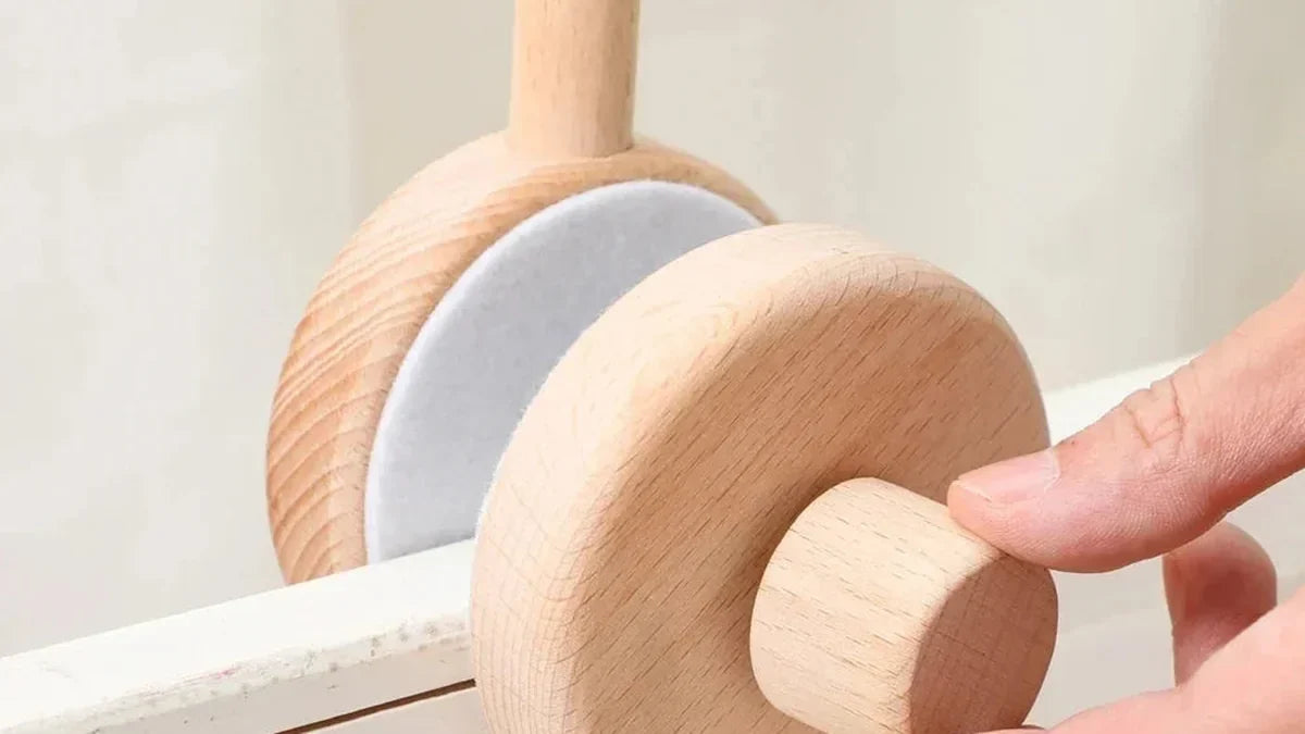 Main qui serre la molette en bois de la pince d'un support de mobile sur la barre d'un lit de bébé