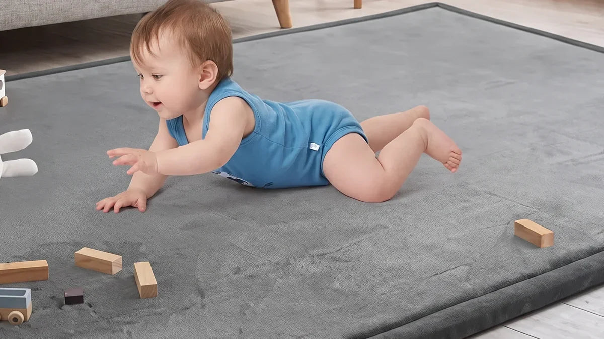 Bébé à plat ventre sur un tapis d'éveil gris en velours, une main tendue vers des cubes en bois