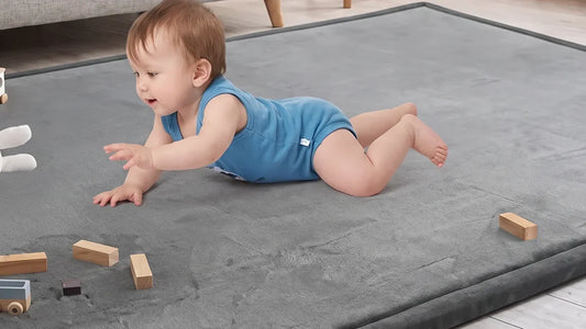 Bébé à plat ventre sur un tapis d'éveil gris en velours, une main tendue vers des cubes en bois