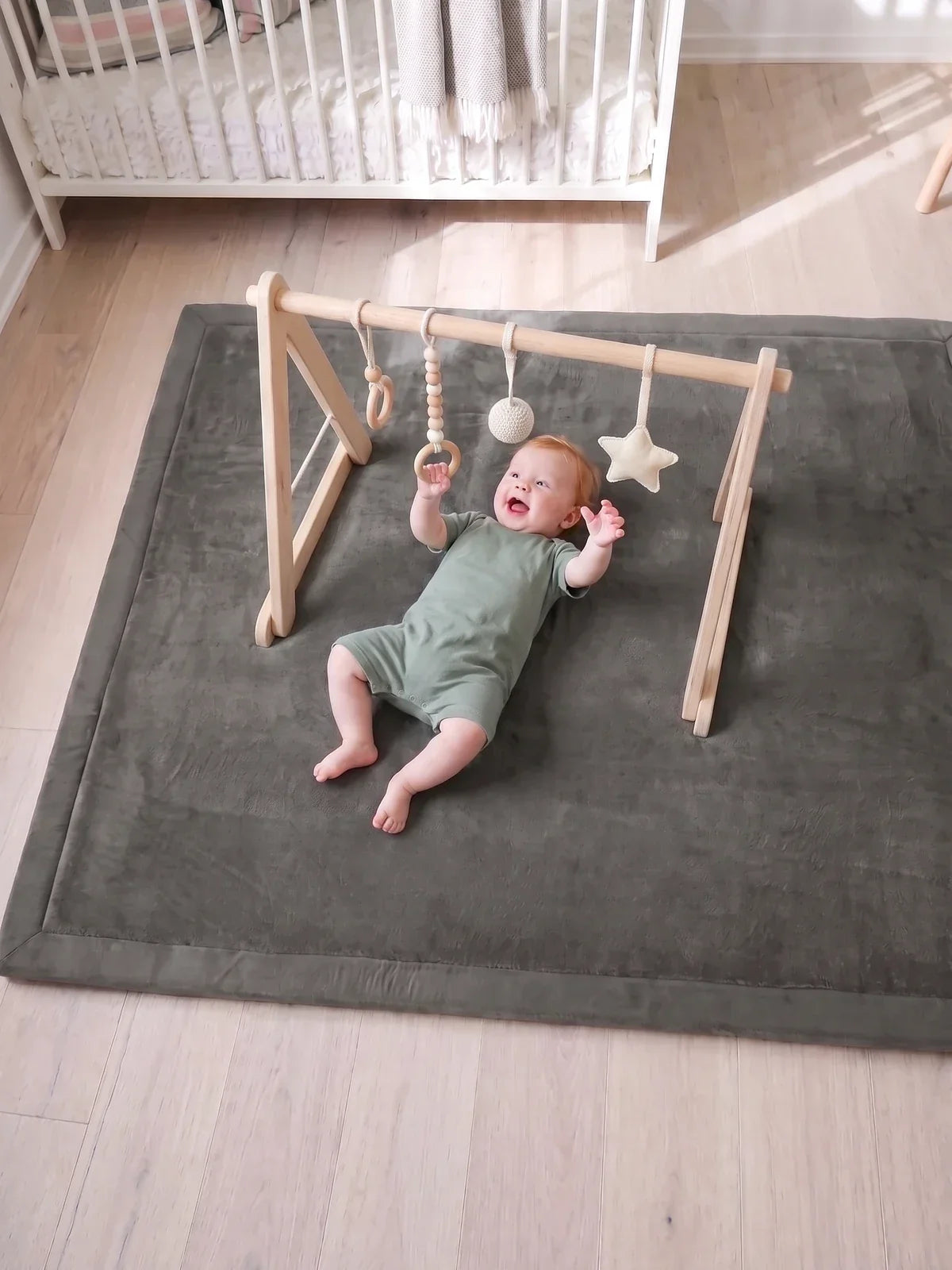 Bébé allongé sur le tapis sous l'arche d'éveil en bois