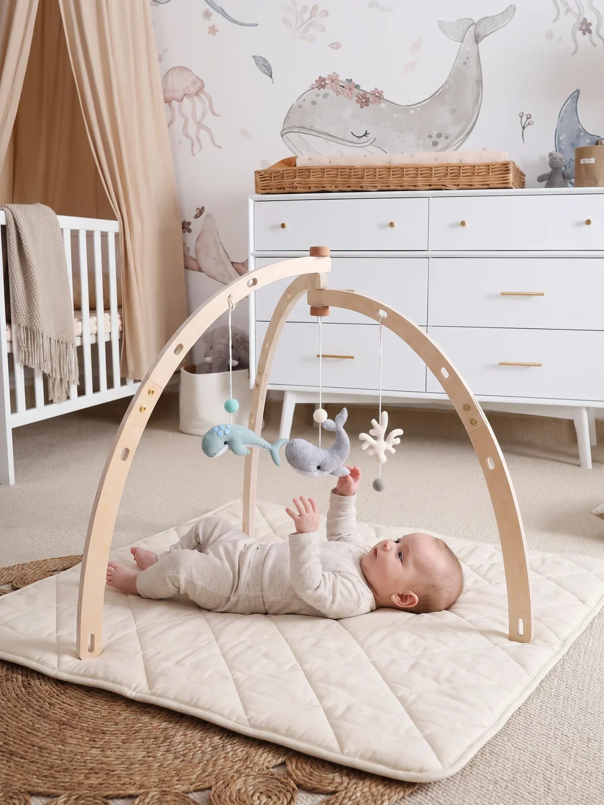 Bébé allongé sur le dos sous l'arche d'éveil, jouets en feutrine suspendus, dans un salon