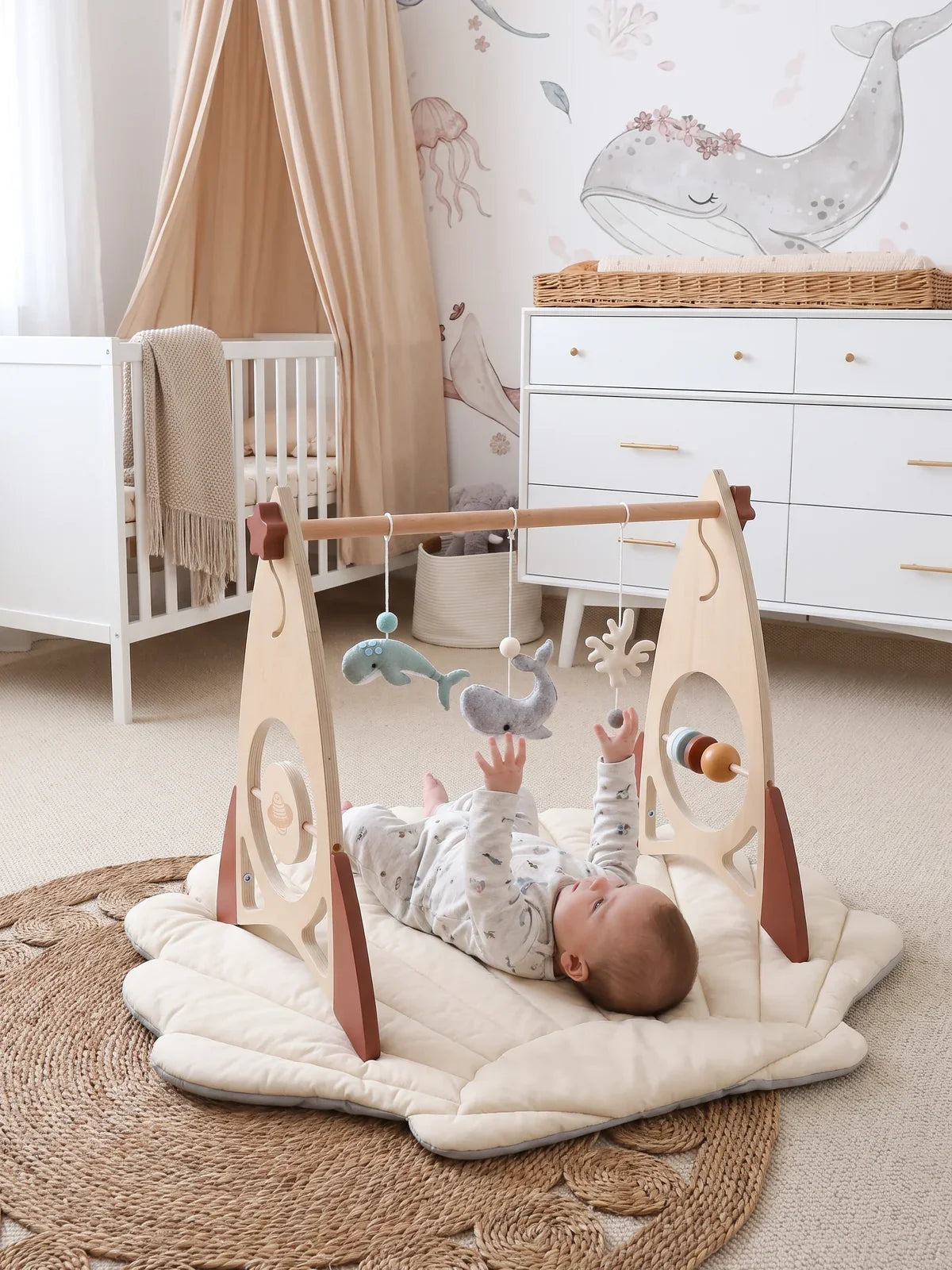 Bébé allongé sur le dos sous l'arche d'éveil, jouets en feutrine suspendus, dans un salon