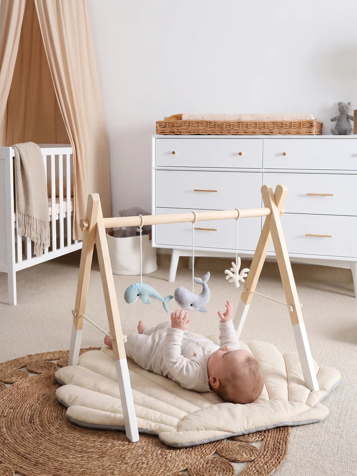 Bébé allongé sur le dos sous l'arche d'éveil, jouets en feutrine suspendus, dans un salon
