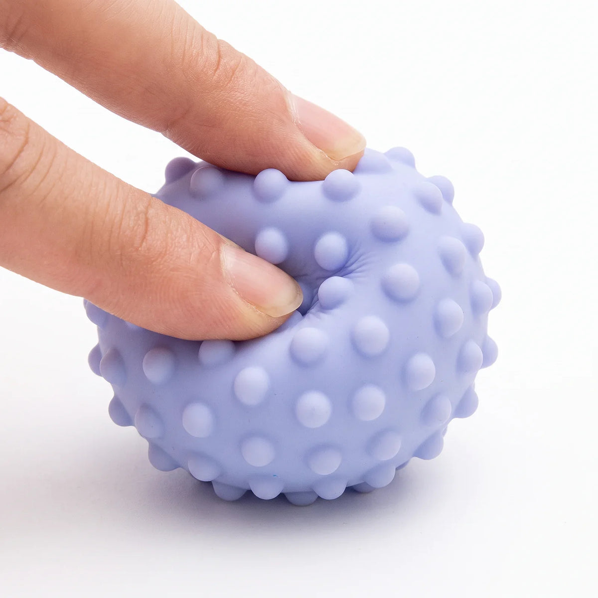 Deux doigts pressent une balle : le silicone s'enfonce puis reprend sa forme
