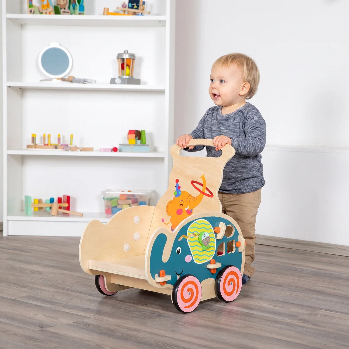 Un enfant debout pousse le chariot de marche en bois, les deux mains sur la poignée