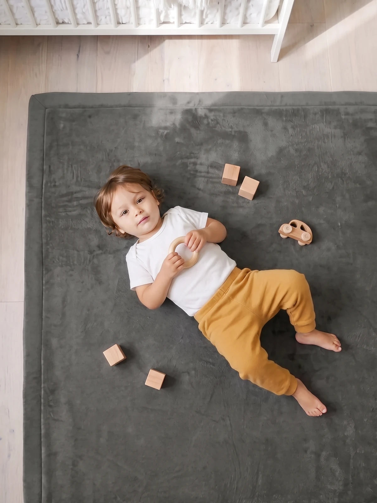 Bébé allongé sur le dos sur le tapis d'éveil, vu de dessus, blocs et voiture en bois