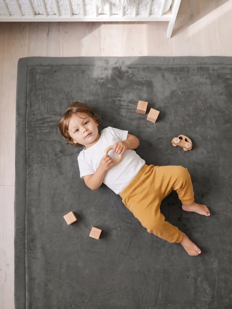 Bébé allongé sur le dos sur le tapis d'éveil, vu de dessus, blocs et voiture en bois