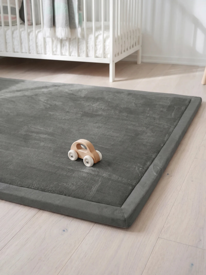 Coin du tapis d'éveil au ras du sol, velours et rebord plat, petite voiture en bois