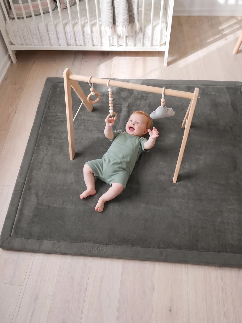 Bébé allongé sur le tapis d'éveil sous l'arche en bois