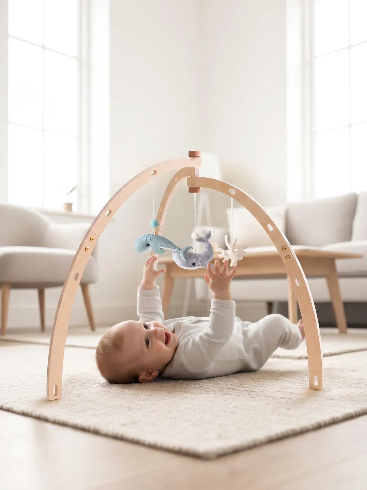 Bébé allongé sur le dos sous l'arche d'éveil, dans un salon