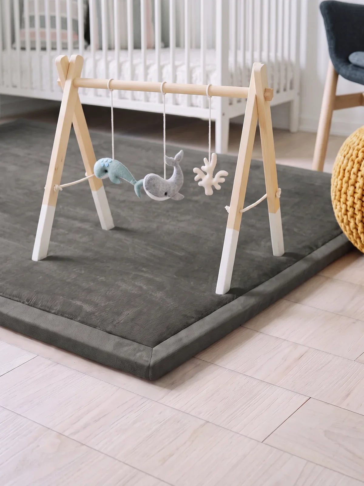 Arche d'éveil en bois, pieds blancs posée sur le tapis d'éveil gris, jouets en feutrine suspendus