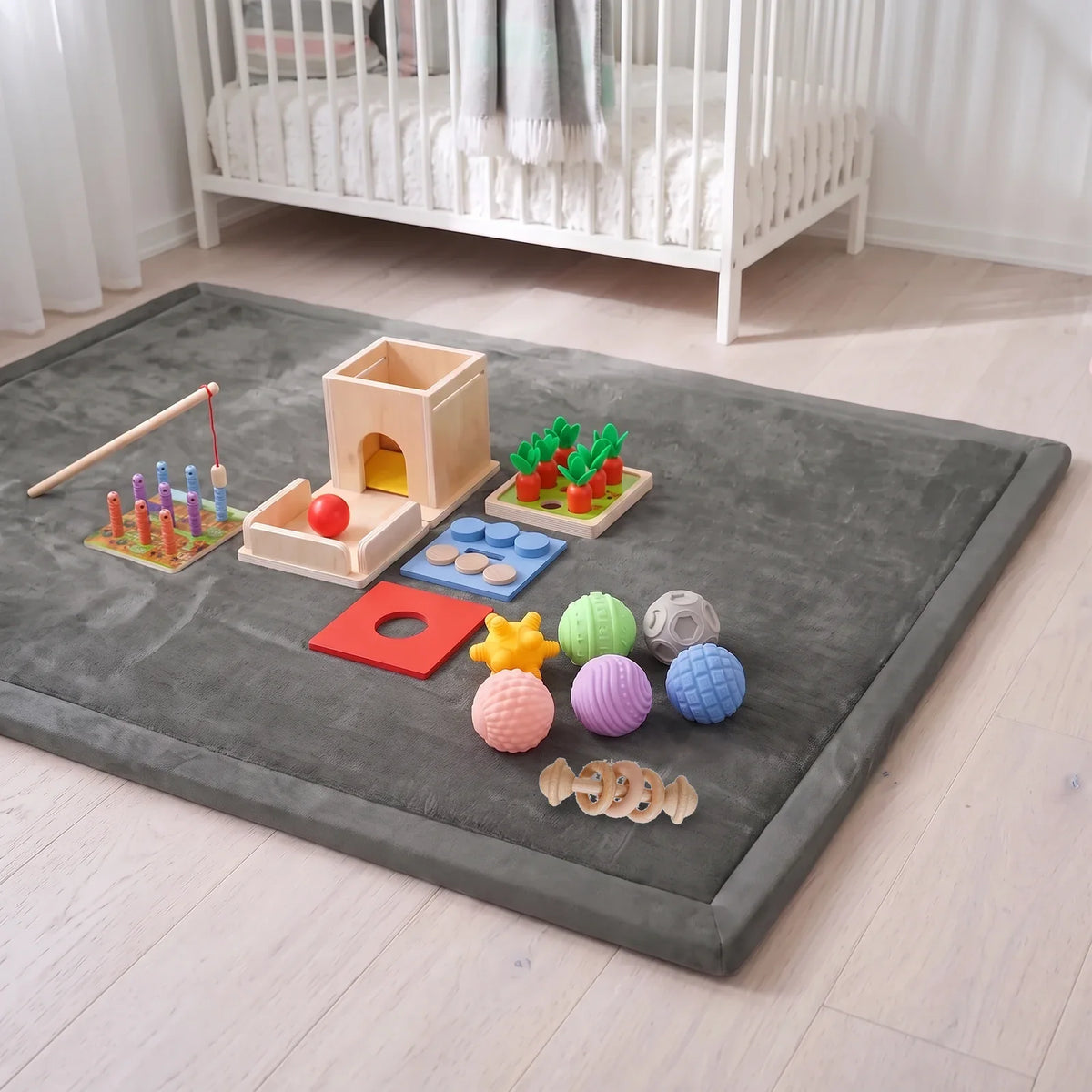 Le tapis d'éveil gris dans une chambre, avec la boîte de permanence 4 en 1, les six balles sensorielles et le hochet à anneaux posés dessus
