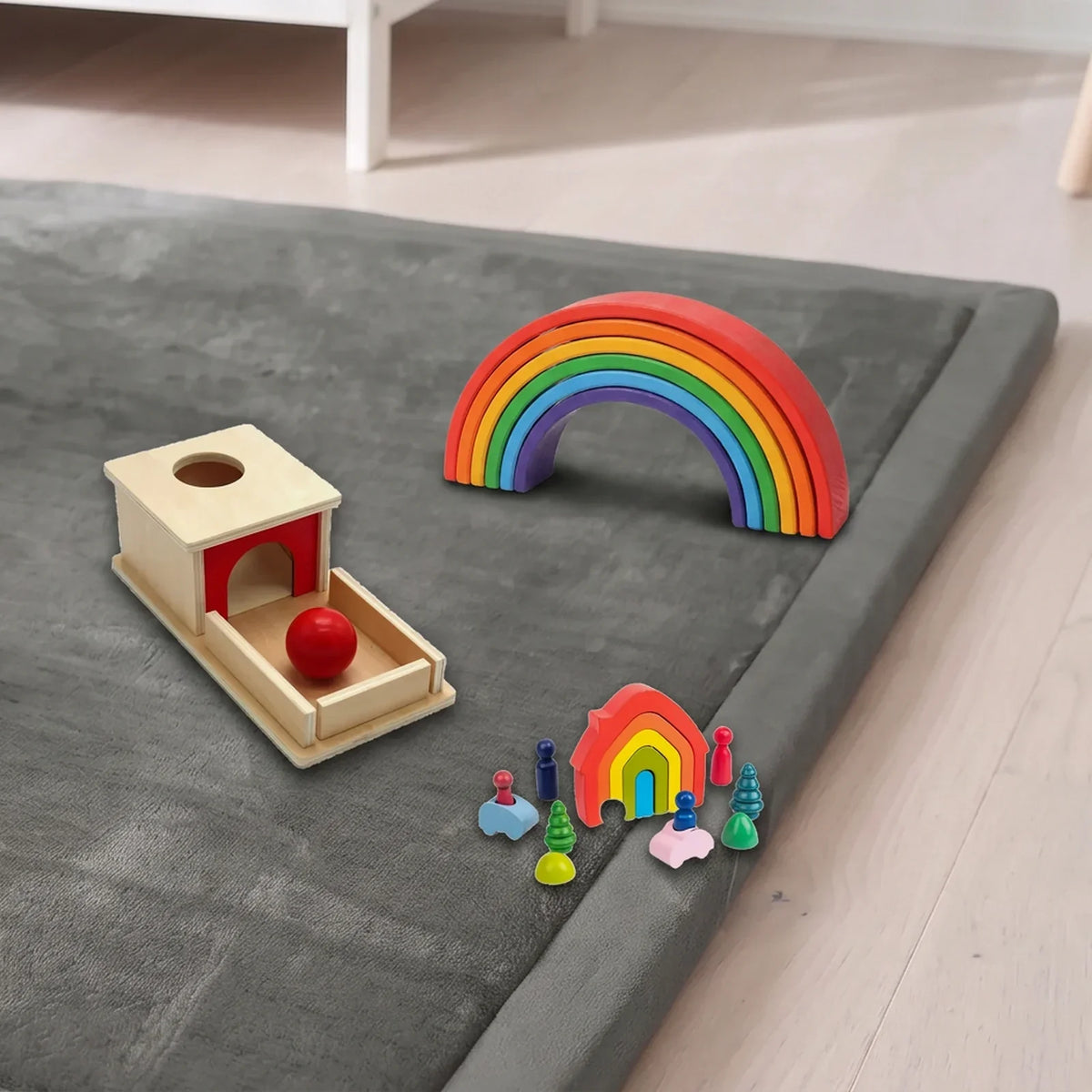 Le tapis d'éveil gris dans une chambre, avec la boîte à balle, l'arc-en-ciel et la maison gigogne posés dessus